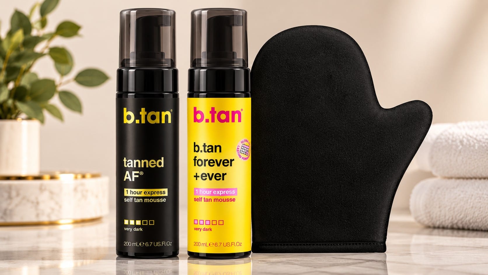 b.tan Tanned AF and Forever + Ever 1-hour express self-tan mousses in black and yellow bottles beside a black tanning mitt on a marble counter.